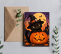 Black cat Halloween greeting card wearing a witch hat with a jack-o-lantern, moon, bats, and haunted house on a kraft envelope